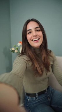 Dikey. Neşeli genç bir kadın neşeli bir şekilde elini sallarken arkadaşlarıyla eğlenceli ve canlı bir video görüşmesi yapıyor, parlak gülüşünü, dostça tavırlarını, mutluluğunu ve bağlantısını gösteriyor. Yüksek