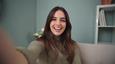 Neşeli genç bir kadın neşeli bir şekilde elini sallarken arkadaşlarıyla eğlenceli ve canlı bir video görüşmesi yapıyor, neşeli gülüşünü ve arkadaş canlısı tavrını sergiliyor, mutluluk ve bağlantı için mükemmel. Yüksek