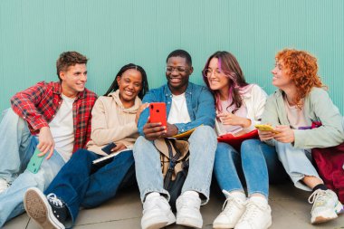 Smartphone 'un mavi bir turkuaz duvarın karşısında oturmasından büyülenmiş çeşitli genç kolej öğrencileri kaynaşıyor ve birlikte bir anı paylaşıyorlar. Gençler cep telefonuyla bakıyorlar. Yüksek