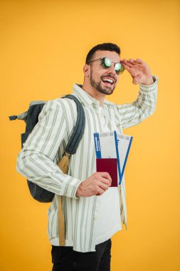 Excited young man saluting while holding passport and boarding passes ready for a upcoming flight to a new adventure in the destination with a cheerful attitude and a sense of thrill and anticipation clipart