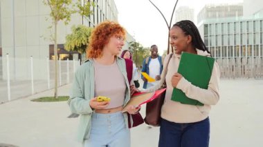 Çeşitli öğrencilerden oluşan neşeli bir grup, akademik başarı ve dostluğa doğru yaptıkları kampüs yolculuklarında gülüşlerini ve gülüşlerini paylaşırken klasörler ve defterlerle birlikte yürüyorlar. Yüksek