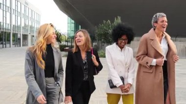 Bir grup profesyonel kadın, hareketli bir sohbete dalarken ve şık bir iş elbisesi içinde güvenlerini ve yoldaşlıklarını gösterirken yüzlerini neşe ve neşe ile aydınlatırlar.