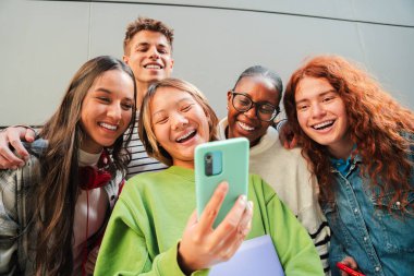 Neşeli bir grup genç arkadaş, akıllı telefonlarıyla fotoğraf çekerken kahkaha ve neşe paylaşıyor, birlikte keyifli bir anın tadını çıkarıyor ve cep telefonlarıyla özel anılarını yakalıyorlar.