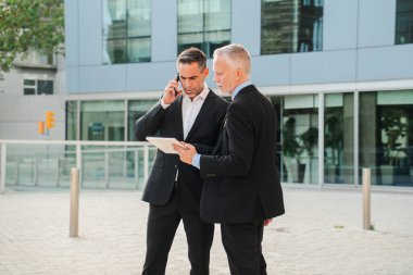 İki işadamı telefonda ciddi bir konuşma yaparken, diğeri de bir tablet cihazında ayrıntıları inceleyerek profesyonelliği ve iş birliğini gözler önüne seriyor.