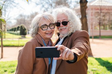 Neşeli son sınıf çifti, akıllı telefonlarıyla mutlu bir selfie çekiyor, birlikte güzel bir an paylaşıyorlar, birbirlerine olan sevgilerini ve mutluluklarını gösteriyorlar, bu uzun süreli anıları yaratıyorlar.