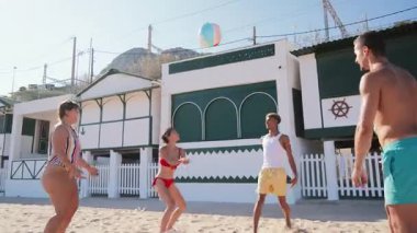 Neşeli bir arkadaş grubu kumsalda güneşli bir günün tadını çıkarıyor, renkli bir topla oynuyor, mutluluk ve enerji saçıyor ve güzel bir kıyı ortamında kahkaha ve eğlence anlarını paylaşıyorlar.