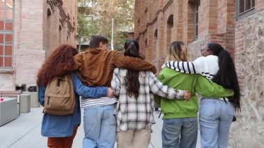 Birbirlerini kucaklarken mutlu mesut yürüyen bir grup genç, canlı bir üniversite topluluğundaki öğrenciler arasındaki neşe dolu arkadaşlık ve birlik bağını yansıtıyor.