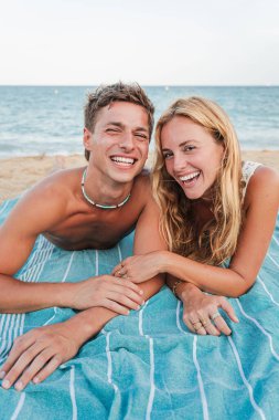 Mutlu çift kumsalda birlikte dinleniyor, yumuşak bir havluya uzanıyor, kahkahalarla gülüyor ve eğleniyorlar, dalgaların çarpma sesi ve tenlerindeki güneşin sıcaklığıyla.