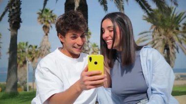 Mutlu genç bir çift, neşeli bir atmosferde akıllı bir telefonla selfie çekerek keyifli bir anı yakalıyor..