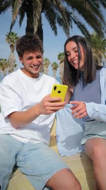 Dikey. Mutlu genç bir çift, neşeli bir atmosferde akıllı bir telefonla selfie çekerek keyifli bir anı yakalıyor..