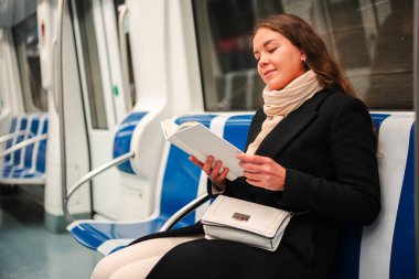 Odaklanmış bir kadın, metro yolculuğu boyunca ilgi çekici bir kitap okumaya, edebiyat zevkini ve toplum içinde seyahat ederken okumanın zenginleştirici deneyimini vurgulamaya dalmıştır.