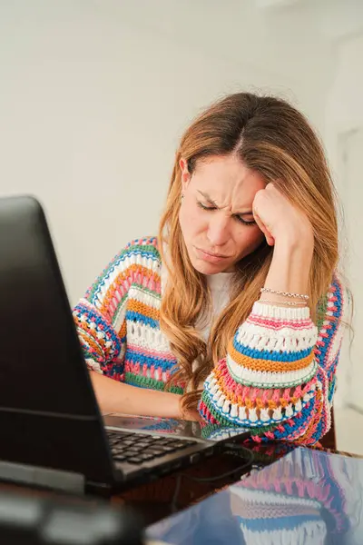 Uzun saçlı stresli bir kadın dizüstü bilgisayarı üzerinde çalışırken gözle görülür şekilde hayal kırıklığına uğruyor. Alnını sıkıntı içinde tutuyor. İşle ilgili sorunların üstesinden gelme çabasını gösteriyor.