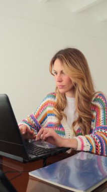 Uzun saçlı stresli bir kadın dizüstü bilgisayarı üzerinde çalışırken gözle görülür şekilde hayal kırıklığına uğruyor. Alnını sıkıntı içinde tutuyor. İşle ilgili sorunların üstesinden gelme çabasını gösteriyor.