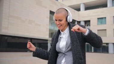 Neşeli bir kadın en sevdiği müzikle neşeyle dans ediyor kulaklık takıyor, ritme kendini kaptırmış ve bulaşıcı bir mutluluk ve özgürlük duygusuyla dışarıda vakit geçiriyor..