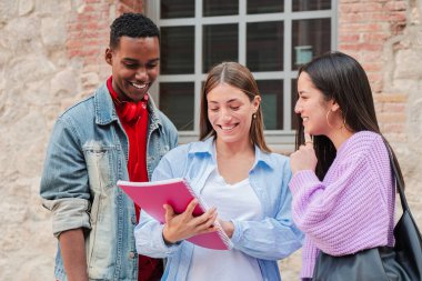 Üç hevesli genç arkadaştan oluşan bir grup birlikte bir defter incelerken keyifle fikir paylaşıyor, dostluklarını ve açık havada canlı sohbetlerini sergiliyorlar..