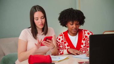 İki neşeli kadın akıllı telefon kullanırken, neşeli bir etkileşimden zevk alıyorlar, kahkahaları paylaşıyorlar ve heyecan verici mobil uygulamaları keşfediyorlar, arkadaşlığın ve modern hayatın özünü vurguluyorlar.