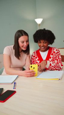 İki neşeli kadın, parlak sarı bir akıllı telefonla etkileşime girerek, kahkahalarını paylaşarak ve büyüleyici bir mobil uygulamayı keşfederek keyifli bir ana kapılıyorlar.