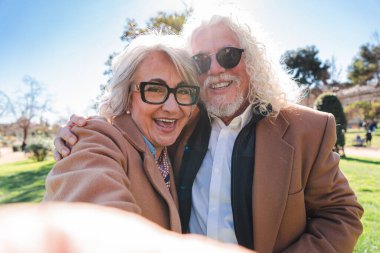 Mutlu yaşlı çift, kahkaha ve neşeyle dolu hatırlanmaya değer bir selfie anı yakalar. Birbirlerine olan güçlü bağlarını ve sevgilerini yansıtırlar.