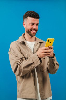 Akıllı telefonuyla meşgul olan neşeli bir adam, teknoloji ve mobil uygulamalarla etkileşime girerken neşeli bir yüz ifadesi sergiliyor, modern hayattaki insanlar ve cihazlar arasındaki bağlantıyı vurguluyor.