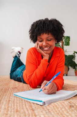 Yaratıcı sürecinden ve çalışmalarından zevk alırken, yerde yatarken, olumlu ve motivasyon saçan, defterine yazmakla meşgul neşeli bir kız mükemmel bir anın görüntüsünü yakalıyor.