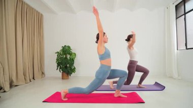Barışçıl bir mekanda, iki kadın yoga pozları veriyor, fitness ve farkındalığa olan bağlılıklarını sergiliyorlar. Dengelerine ve nefeslerine yoğunlaşıyorlar. Gücü somutlaştırıyorlar.