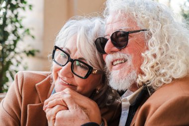 Sevgi dolu yaşlı bir çift sıcak ve sevecen bir anı paylaşırken el ele tutuşuyorlar, neşe ve bağlantı yayıyorlar, güzel bir terasta romantik bir buluşmada aşklarını kutluyorlar