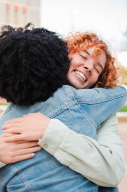 İki neşeli arkadaş sevinçle kucaklaşıyorlar. Sıcak ve dokunaklı bir an yaşıyorlar. Bu güzel etkileşimde güçlü bağlarını ve mutluluklarını ifade ediyorlar..