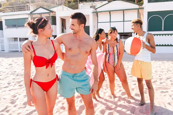 Neşeli bir arkadaş grubu kumsalda keyifli bir gün geçiriyorlar, neşeli aktiviteler yapıyorlar ve kahkahalar atıyorlar sıcak güneşin ve kumlu sahildeki güzel kıyı şeridinin tadını çıkarıyorlar..