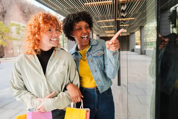 İki neşeli kadın alışveriş yaparken keyifli bir anı paylaşıyor. Birbirlerine ilgi çekici bir şeyi gösterip eğleniyorlar. Yeni keşifler yaparken mutlulukları bulaşıcıdır..