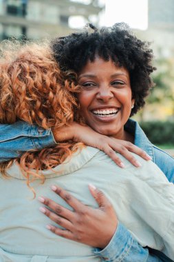 İki neşeli kadın birbirine sıkıca sarılıyor, sevgiyi ve mutluluğu yansıtan parlak gülümsemeleri paylaşıyor, dostluğun ve bağlantının güzelliğini yürekten bir sevgi anında sergiliyorlar..