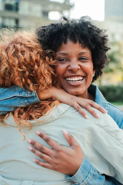 İki neşeli kadın birbirine sıkıca sarılıyor, sevgiyi ve mutluluğu yansıtan parlak gülümsemeleri paylaşıyor, dostluğun ve bağlantının güzelliğini yürekten bir sevgi anında sergiliyorlar..