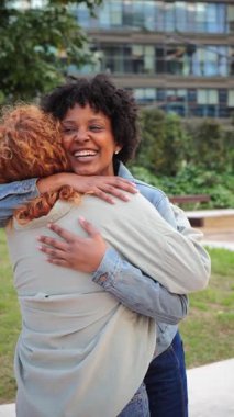 İki neşeli kadın birbirine sıkıca sarılıyor, sevgiyi ve mutluluğu yansıtan parlak gülümsemeleri paylaşıyor, dostluğun ve bağlantının güzelliğini yürekten bir sevgi anında sergiliyorlar..