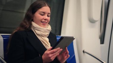 Metroda otururken e-okuyucusuna kitap okumaya dalmış bir kadın, günlük seyahati sırasında edebiyat zevkini yansıtan odaklanmış ve sakin bir ifade sergiliyor.