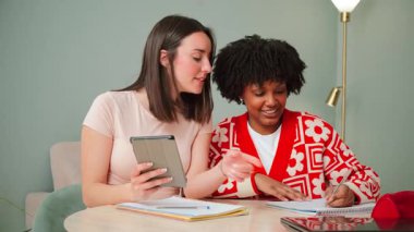 İki hevesli genç kadın, bir tablet kullanırken ve fikirleri neşeyle paylaşırken, üretken bir çalışmada aktif katılımlarını ve etkili takım çalışmalarını sergiliyorlar.