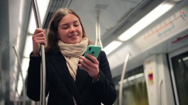 Metroda seyahat ederken akıllı telefonunu kullanan, seyahati sırasında teknolojiye olan bağlılığını vurgulayan, mobil uygulamaların günlük seyahat entegrasyonunu gösteren odaklanmış bir kadın.