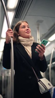 Metroda seyahat ederken akıllı telefonunu kullanan, seyahati sırasında teknolojiye olan bağlılığını vurgulayan, mobil uygulamaların günlük seyahat entegrasyonunu gösteren odaklanmış bir kadın.