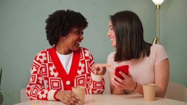İki neşeli dişi, eğlenceli bir videoyu izlerken, arkadaşça bir atmosferde içkilerini yudumlarken kahkaha ve neşeyi paylaşan bir akıllı telefondan büyülenerek bir araya geldiler..