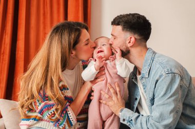 Bu hoş görüntü, sevgi dolu ebeveynlerin neşeli bebeklerine öpücükler yağdırdığı aile sevgisinin saf özünü ve ebeveynliğin tatlılığını yansıtıyor..