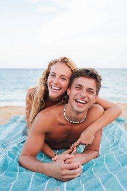 Neşeli bir çift plaj havlusunda uzanıyor. Güneşin altında gülüyor ve birbirlerini kucaklıyorlar. Sakin deniz ve kumlu sahil, birlikte geçirdikleri eğlenceli gün için mükemmel bir zemin oluşturur..