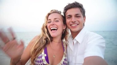 Neşeli bir çift kumsalda harika vakit geçiriyorlar. Güneşli bir yaz gününde parıldayan okyanus dalgalarının yanında gülümseyip el sallarken unutulmaz bir anı yakalıyorlar..