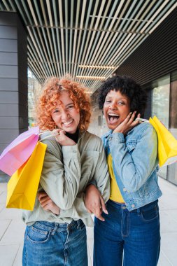 Neşeli kadınlar keyifli bir alışveriş deneyimini paylaşıyorlar, renkli çantalarını ve bulaşıcı gülümsemelerini sergiliyorlar, canlı bir mutluluk anında arkadaşlığı ve heyecanı somutlaştırıyorlar..