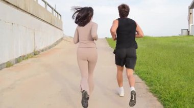 Dinamik çift spor yaparken birlikte güzel bir yolda koşuyorlar, fiziksel aktivite ve arkadaşlık yoluyla sağlık ve refahı teşvik ediyorlar..