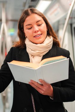 Odaklanmış genç bir kadın, yoğun bir metro treniyle toplu taşımada seyahat ederken sayfalara kendini sokarken neşe ve merak saçan büyüleyici bir kitap okumakla derinden meşgul.