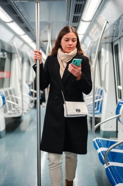 Metroda dururken akıllı telefonunu dikkatle kullanan genç bir kadın cep telefonu uygulamasına dalmış ve toplu taşıma araçlarında seyahat ederken dünya ile bağlantı kurmuş..