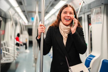 Neşeli bayan yolcu, metroda seyahat ederken akıllı telefonuyla canlı bir sohbete daldı. Ulaşım sırasında günlük hayatındaki iletişim ve bağlantının rahatlığını gösterdi.
