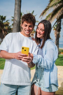 Keyifli bir çift mutlu bir şekilde birlikte akıllı telefonlarını karıştırıyor, güneşli bir günde gülüşlerini ve gülüşlerini paylaşıyor, teknolojinin bağlantılarını ve eğlencesini sergiliyorlar..