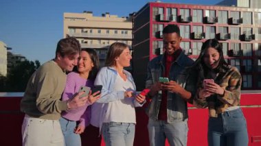 Birlikte eğlenen, akıllı telefonlarına dalmış, kahkaha ve heyecanı paylaşan bir grup arkadaş. Gülüşleri, teknoloji ve dostluk yoluyla bağlanmanın sevincini yansıtıyor..