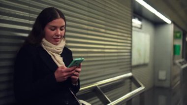 Ulaşım beklerken akıllı telefonunu kullanmaya odaklanmış, uygulamalara dalmış, dijital dünyayı keşfetmiş, teknoloji ve günlük yaşam arasındaki bağlantıyı gözler önüne sermiş bir kadın.