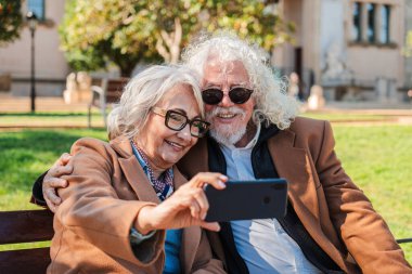 Mutlu son sınıf çifti, mutlu bir şekilde akıllı telefonuyla selfie çekiyor, kahkahalarla, sevgiyle ve iletişimle dolu hoş bir anı yaratıyor ve birlikte güzel bir açık havada özel bir anı paylaşıyorlar.