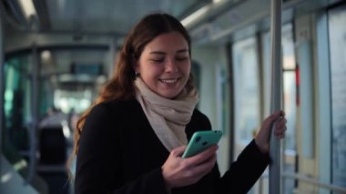 Neşeli bir kadın, bir toplu taşıma aracında dururken akıllı telefonuna odaklanır. Yolcu olarak geçirdiği zamanın tadını çıkarır ve mobil cihazıyla çeşitli uygulamaları inceler.